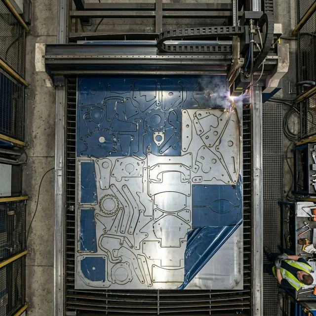Top-down view of an industrial laser cutting bed showing a highly optimized nesting layout with irregular metal parts tightly arranged, featuring common-line cutting and minimal scrape waste